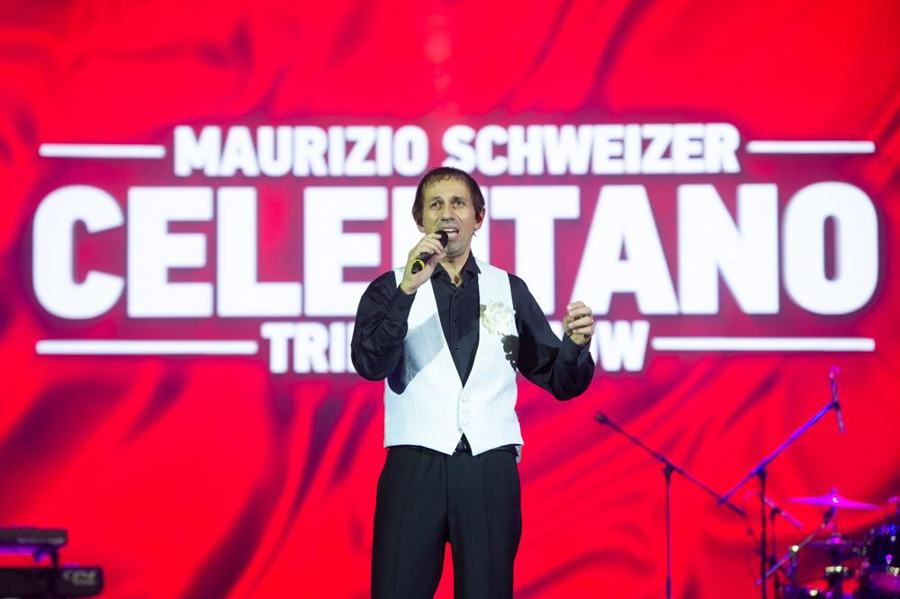 Артист в белом жилете поёт на фоне красного экрана с надписью Celentano Tribute Show